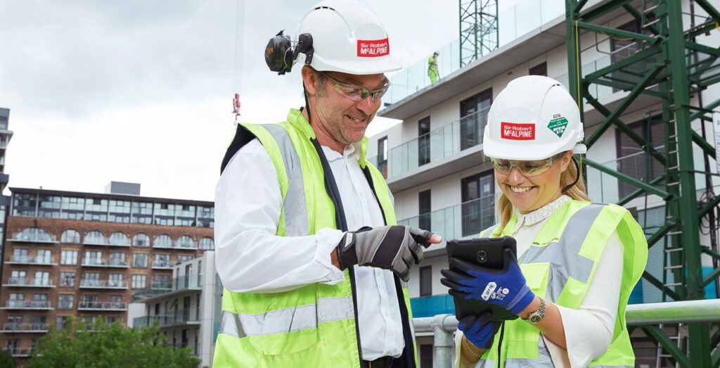 Two construction workers, one male, one female, looking at a tablet